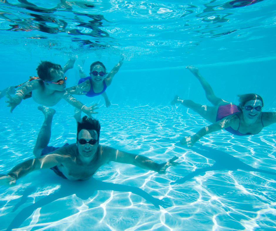 A white family of two adults and two children swimming underwater in a swimming pool.